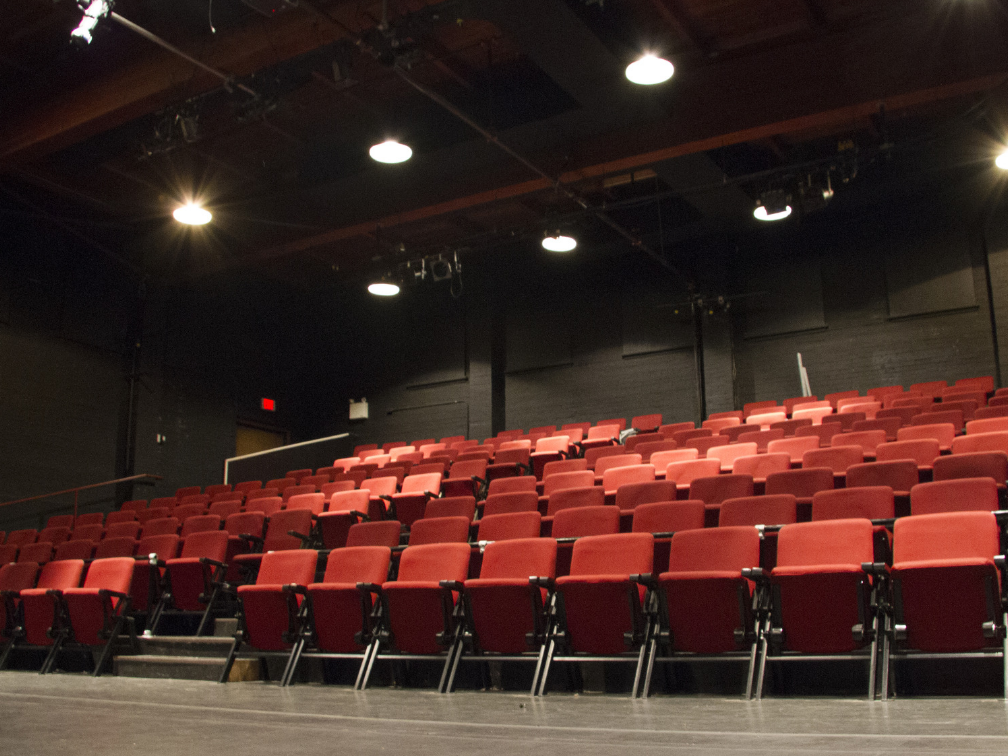 Red theatre seats in rows with bright house lights above