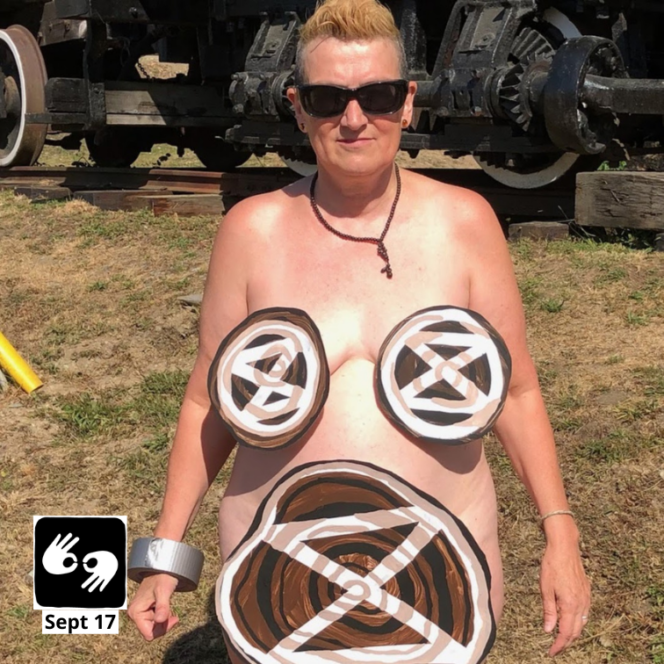 Tasha is standing in front of the BC Forest Discovery Centre wearing only painted tree rings with extinction symbols over her breasts and pubic area.