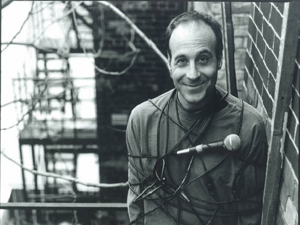 Black & white photo of Paul, standing ona fire escape, wrapped in a microphone cable