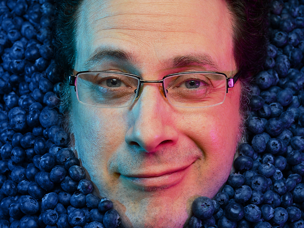 TJ's smiling face, surrounded by blueberries, as if he's lying in a pool filled with the things.