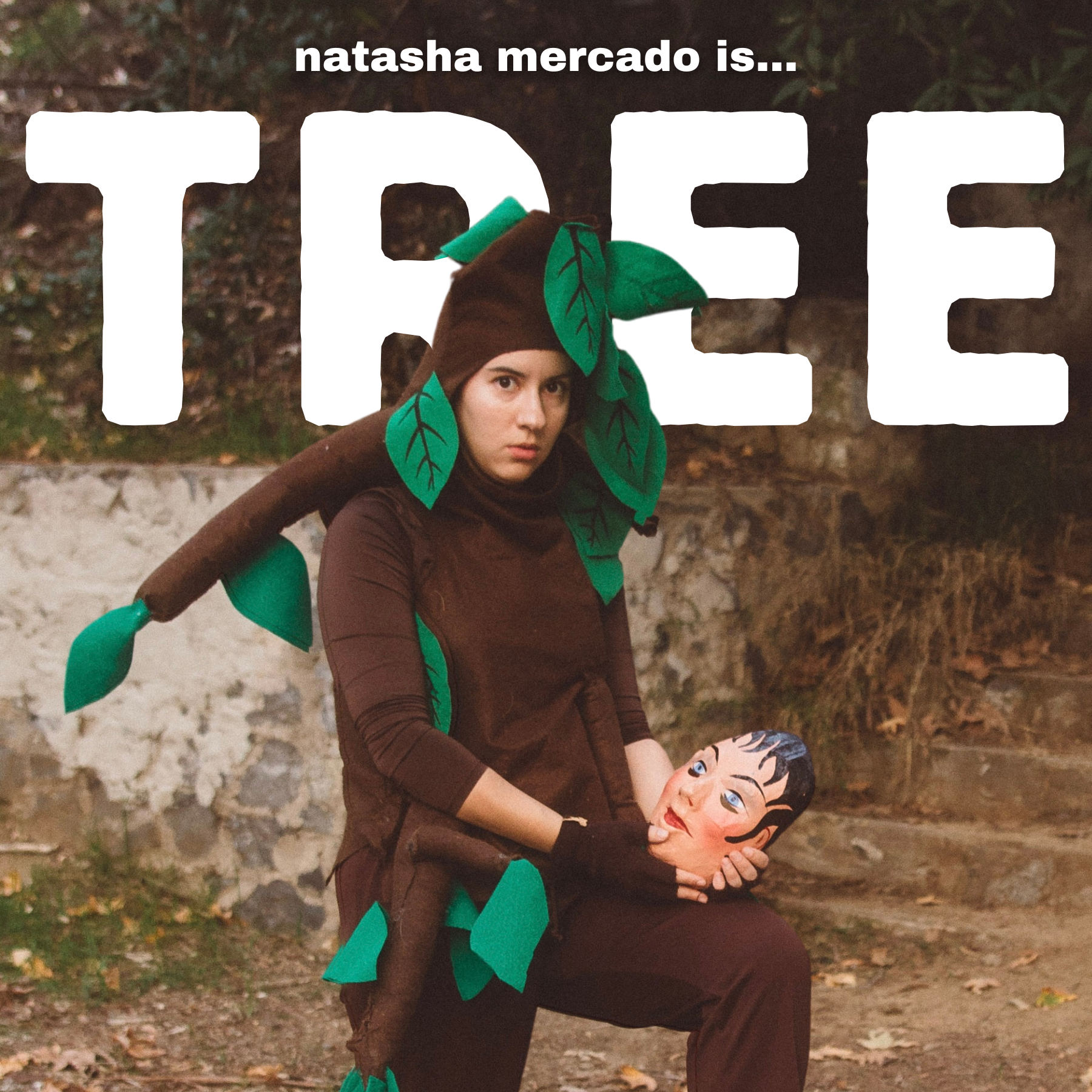 Photo of Natasha Mercado in her Tree Costume holding a "human mask" in nature. Above her, the words-- "natasha mercado is... TREE"
