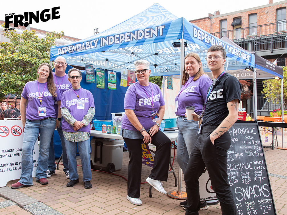 A photo of five Fringe volunteers and one fringe staff memebr at Fringe Preview in Market Square. They are outside, standing against the backdrop of a pop-up tent