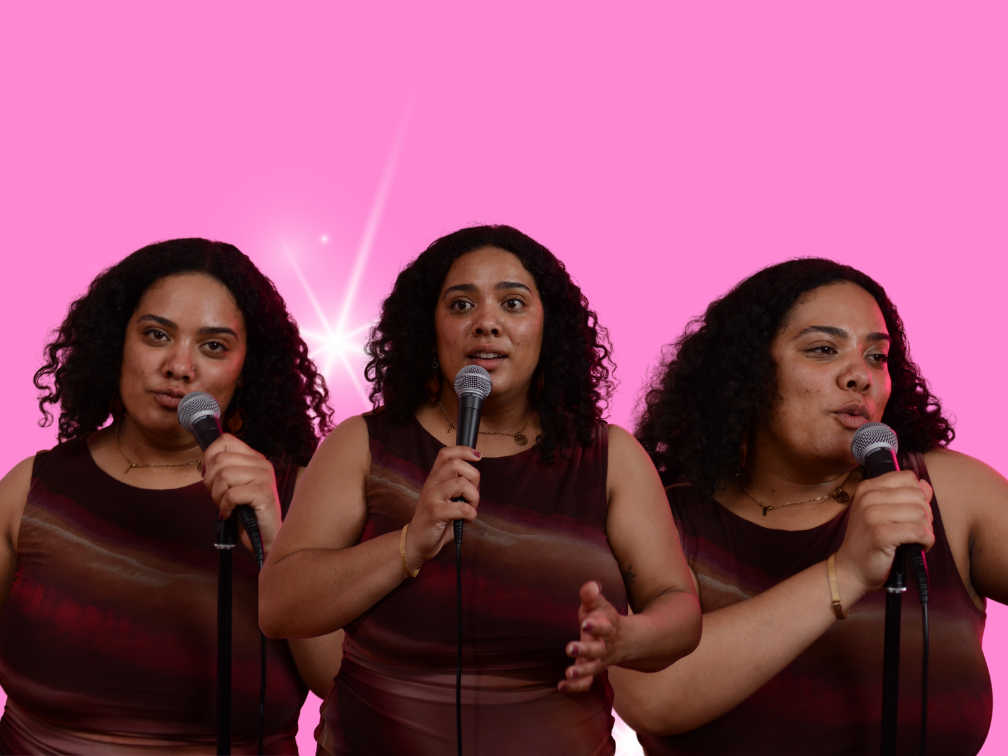 Riel, a thicc Black woman, wearing a black dress, singing into a microphone, mirrored with multiple versions of her behind her with a purple tint.